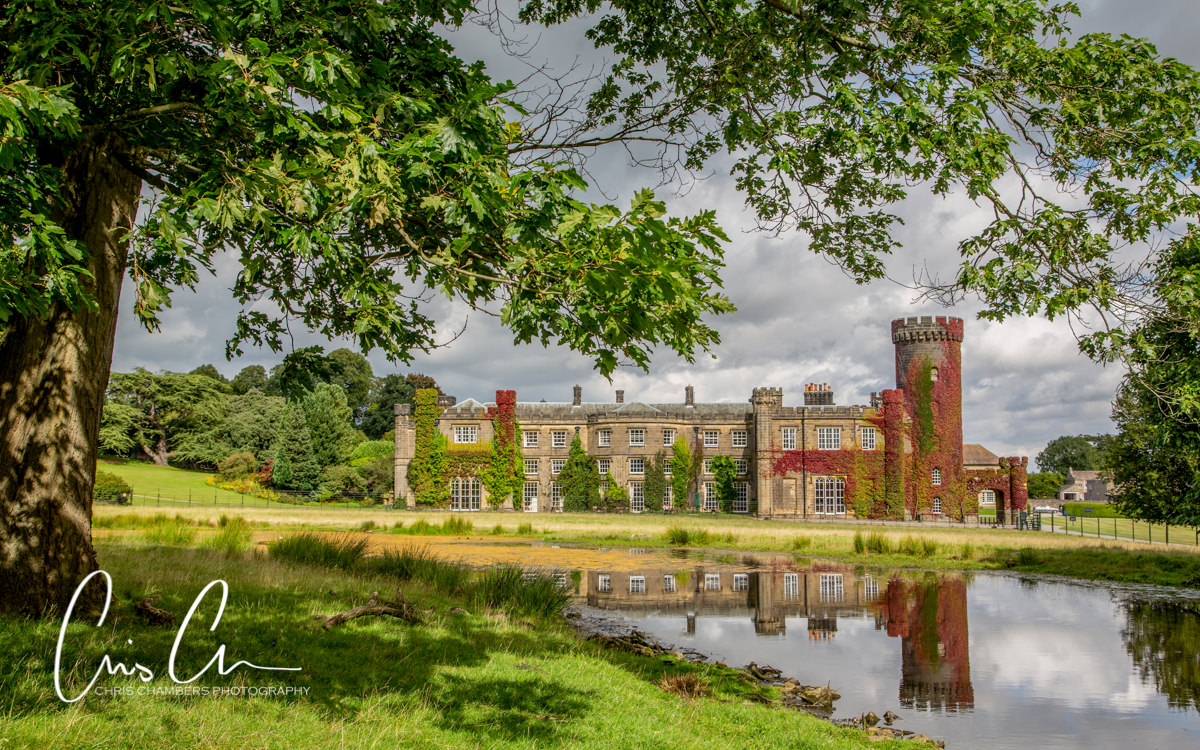 Yorkshire wedding venue, photograph of Swinton Park with reflection in the lake and seasonal red ivy. Swinton Park Wedding Photograph
