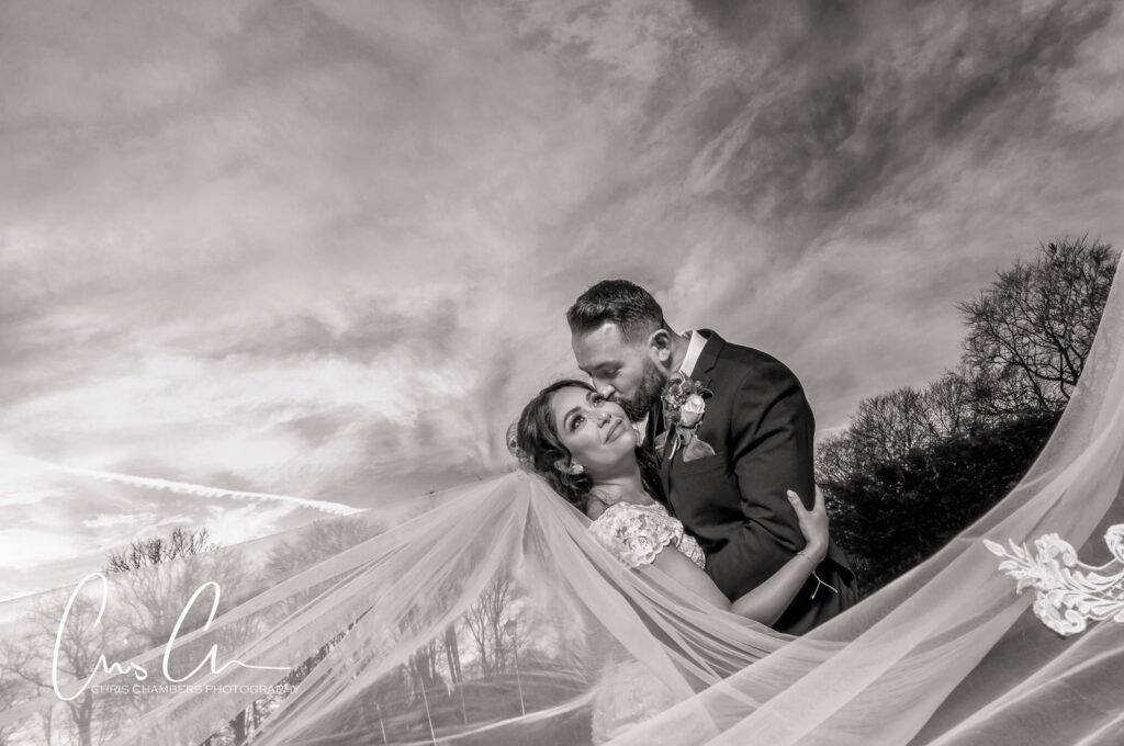 Bride and groom embracing under dramatic sky.