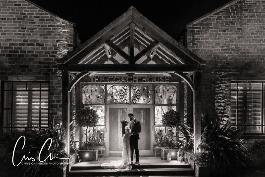 Bride and groom embracing outside illuminated Coach House at night.Manor House Lindley.