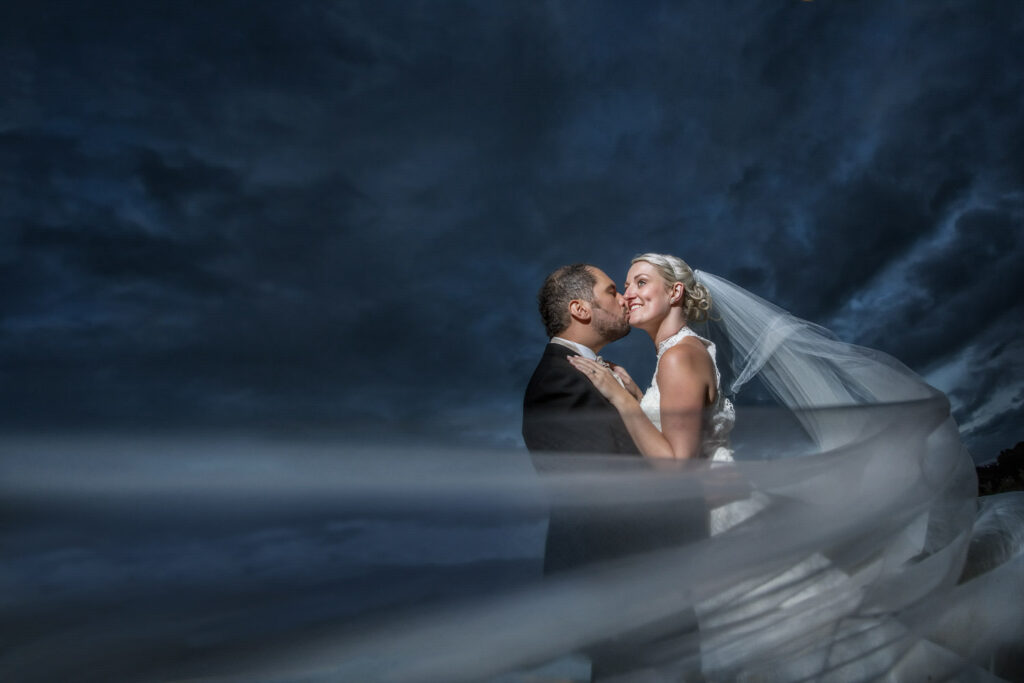 Bride and groom kissing under veil with stormy sky.Chris Chambers Yorkshire wedding photographer