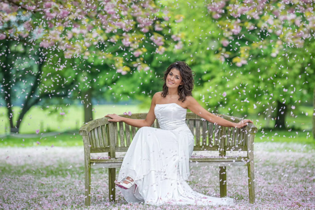 Bride sitting on bench in blossom-filled grounds at Hazlewood Castle. Chris Chambers Yorkshire wedding photographer