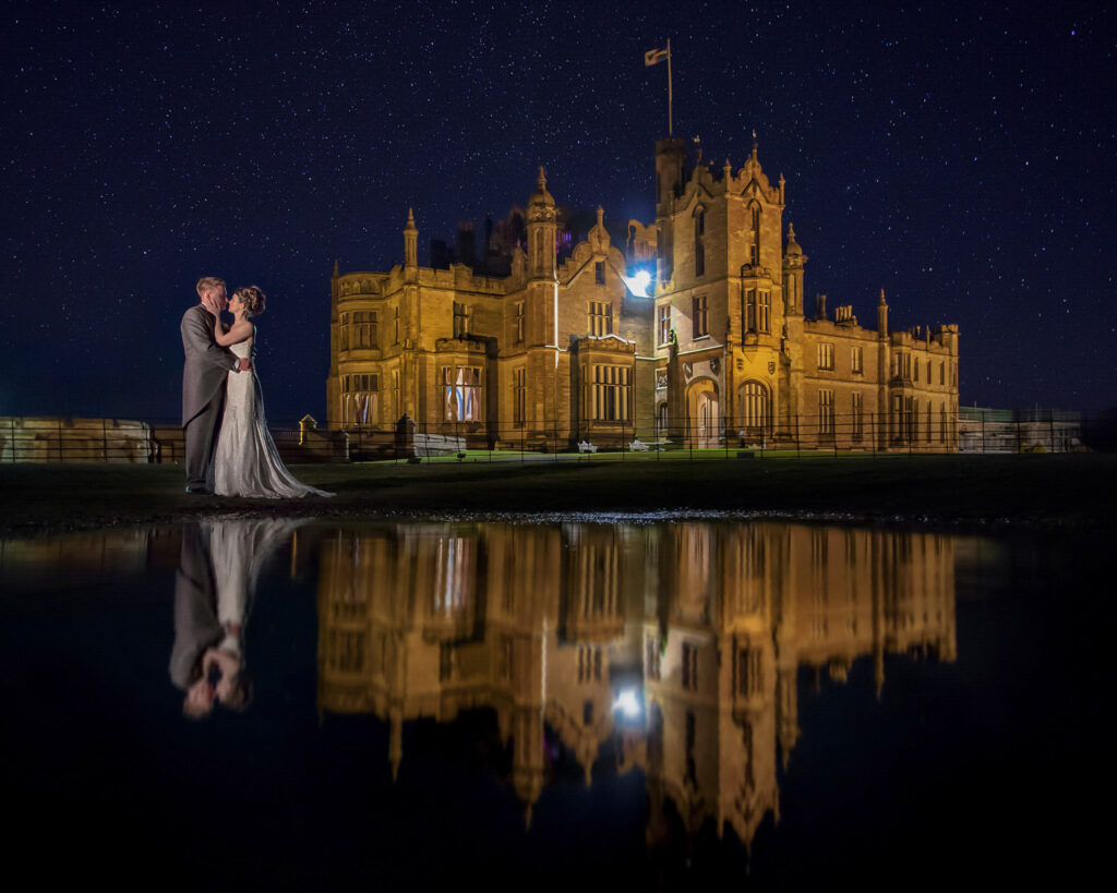 Couple kissing by castle under starry sky with reflection of Allerton Castle