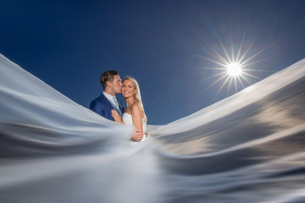 Bride and groom embracing under sunlit sky with long flowing veil. Chris Chambers Yorkshire wedding photographer