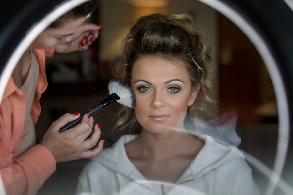 Makeup artist applying cosmetics to woman with ring light reflection