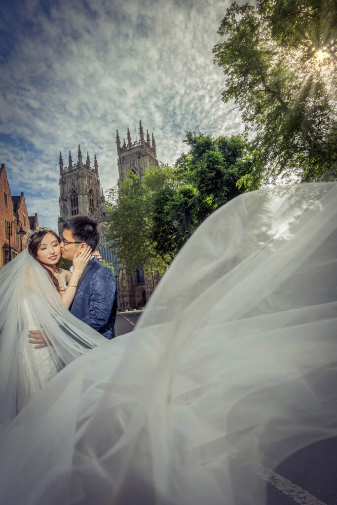 Couple kissing near York Minster with flowing bridal veil.