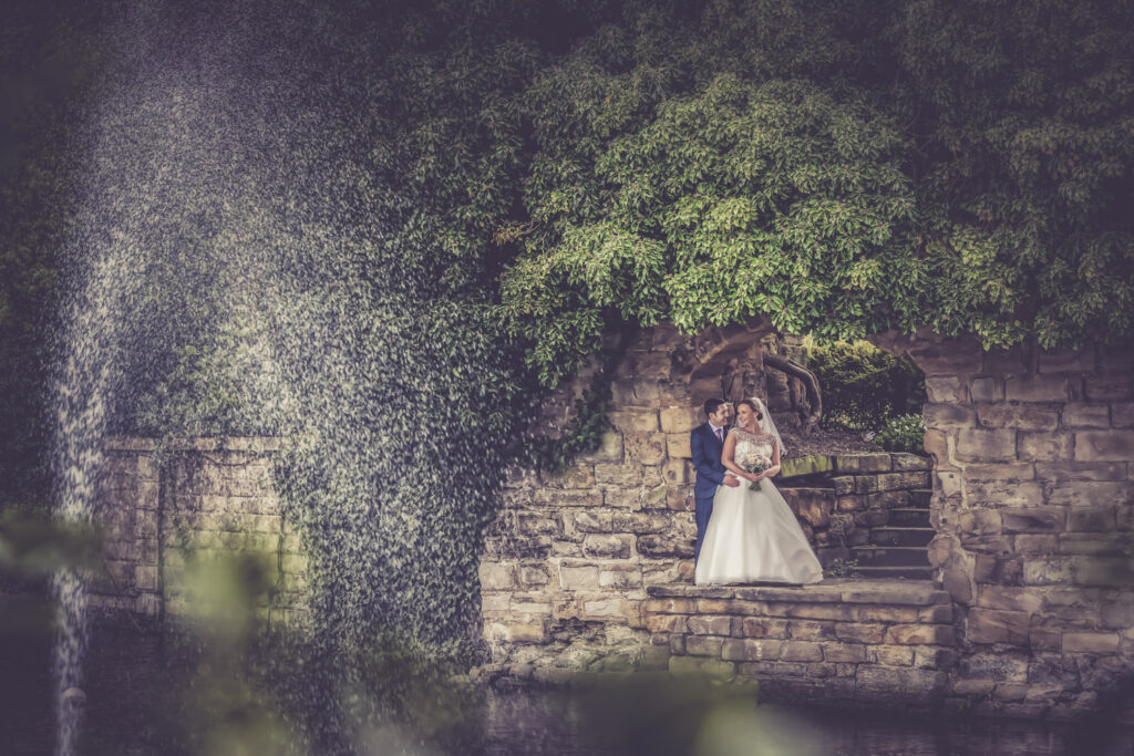 Wedding couple posing by ivy-covered stone wall fountain at Walton hall Wakefield