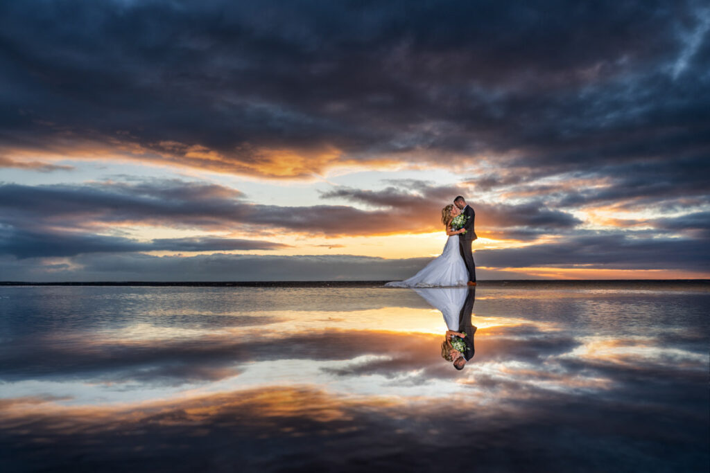 Couple kissing, sunset reflection on water, dramatic sky.