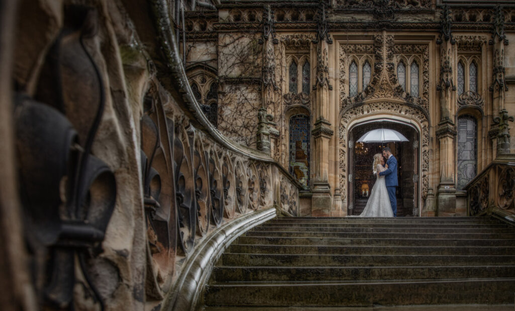 A wet and raint carlton towers wedding day. Couple stand in the doorway under an umbrella.