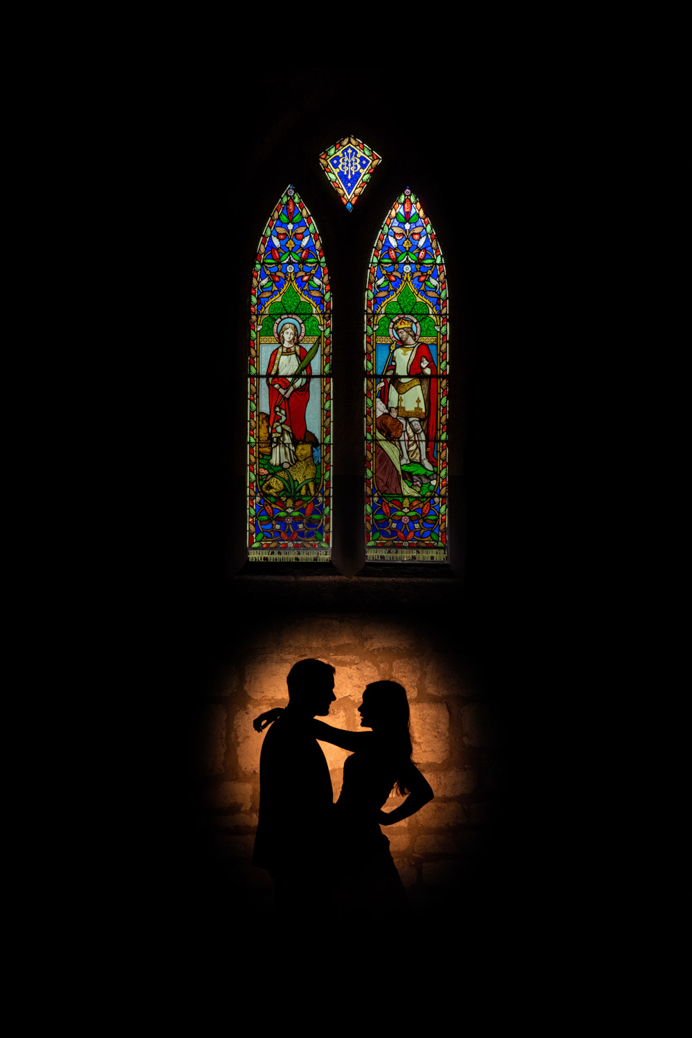 Bride and groom Silhouetted against stained glass window at Hazlewood Castle