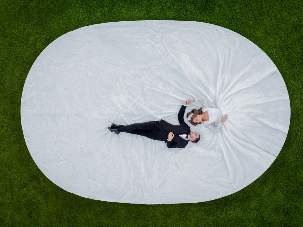 Top down wedding photograph of a bride and groom laying on the grass with a big wedding dress