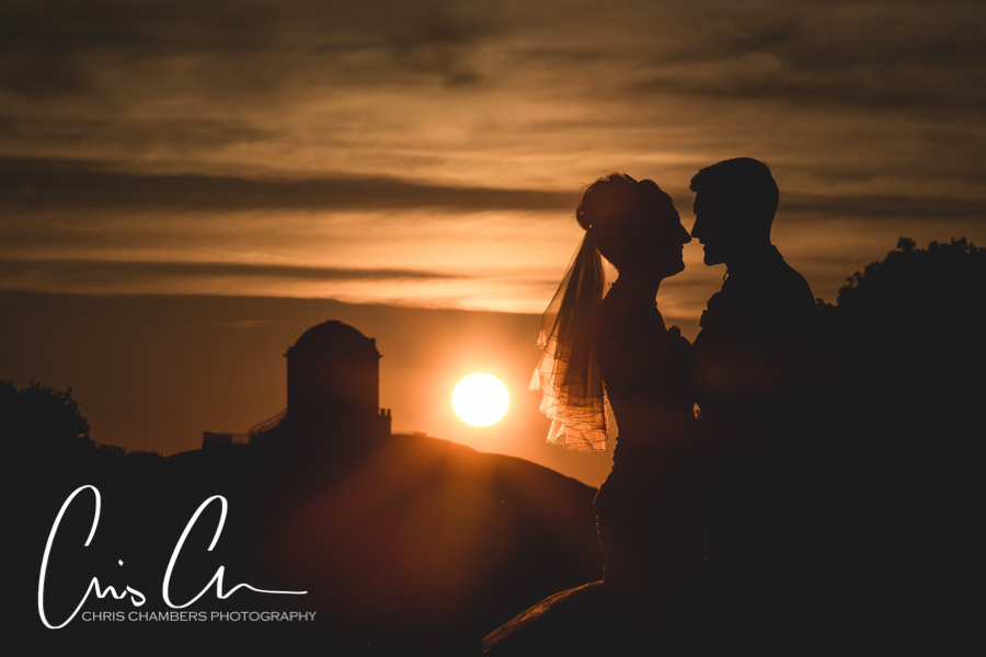 Sunset at an Allerton Castle wedding, Bride and groom silhouetted with a setting sun and the Folly in the background