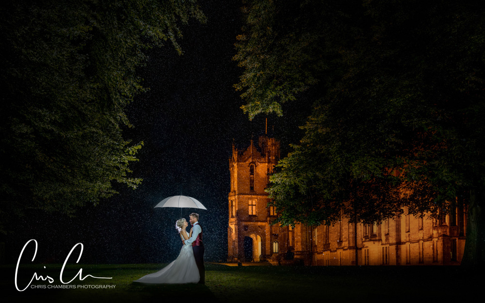 After dark in the rain at Allerton Castle producing amazing wedding photographs, Bride and groom outside with a white umbrella in the rain at Allerton Castle