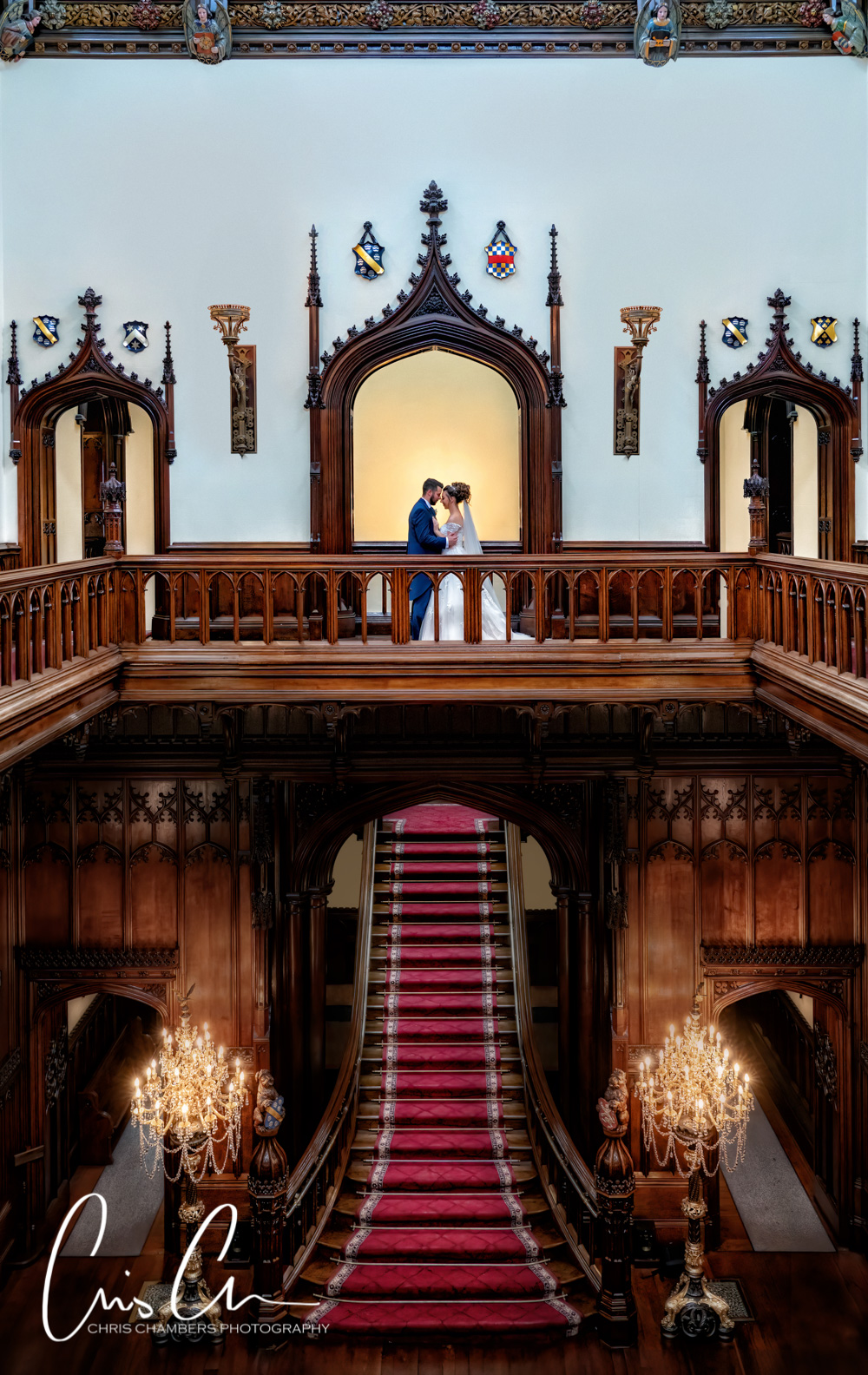 Bride and groom standing above the staircase and gallery at Allerton Castle North Yorkshire. Award winning wedding photograph from the Guild of Photographers