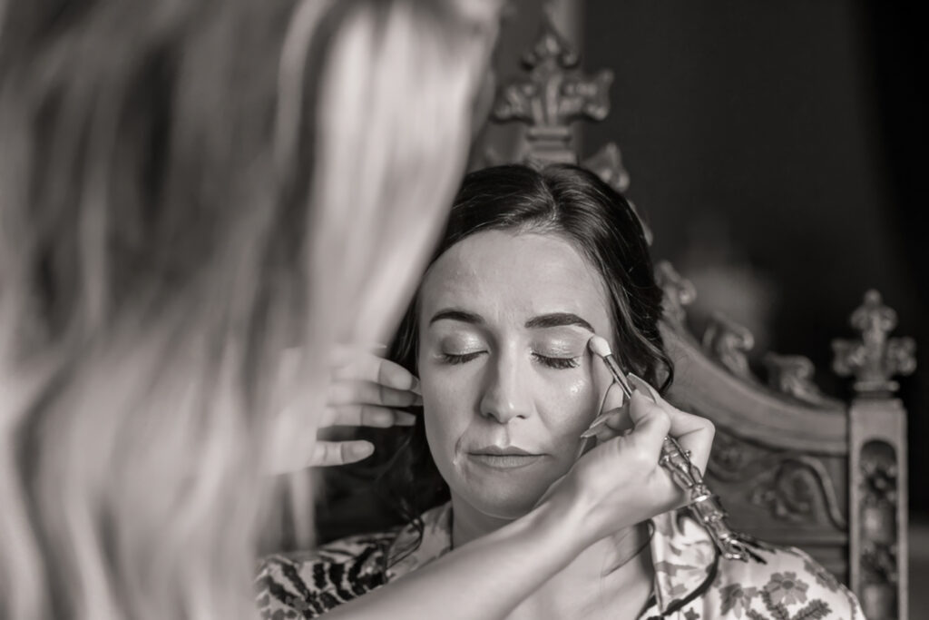 Makeup artist applying eyeshadow on woman, black and white photo. Allerton Castle wedding photographs
