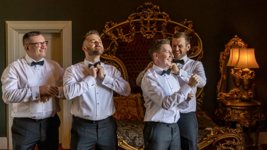 Groomsmen adjusting bow ties in elegant room. Allerton Castle wedding photographs