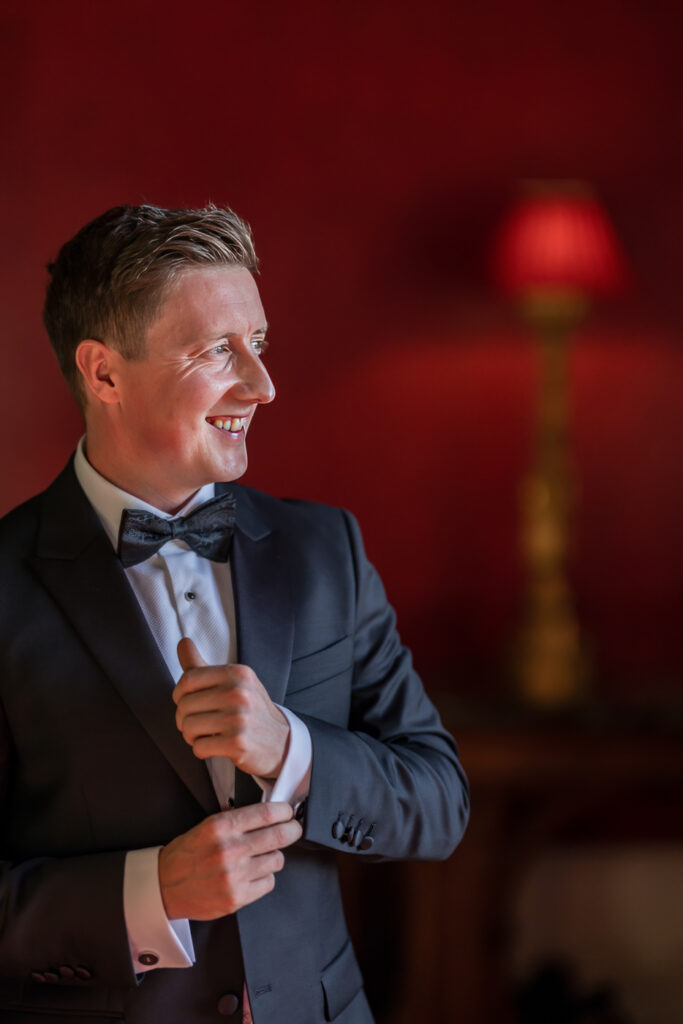 Man smiling in suit with red background. Allerton Castle wedding photographs