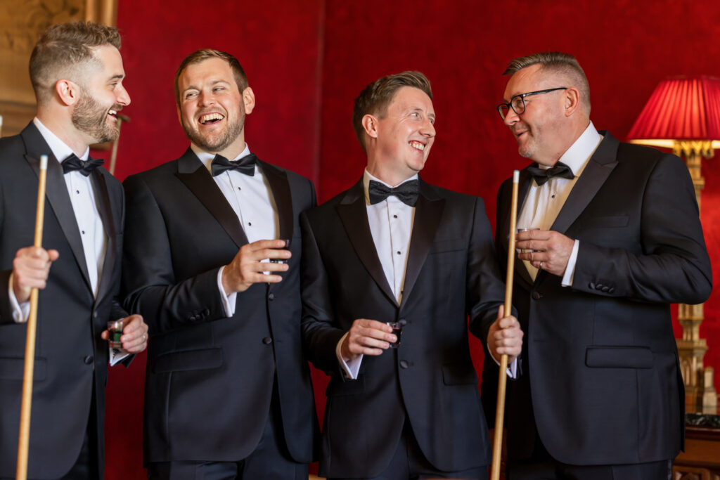 Four men in tuxedos laughing with billiard cues. Allerton Castle wedding photographs
