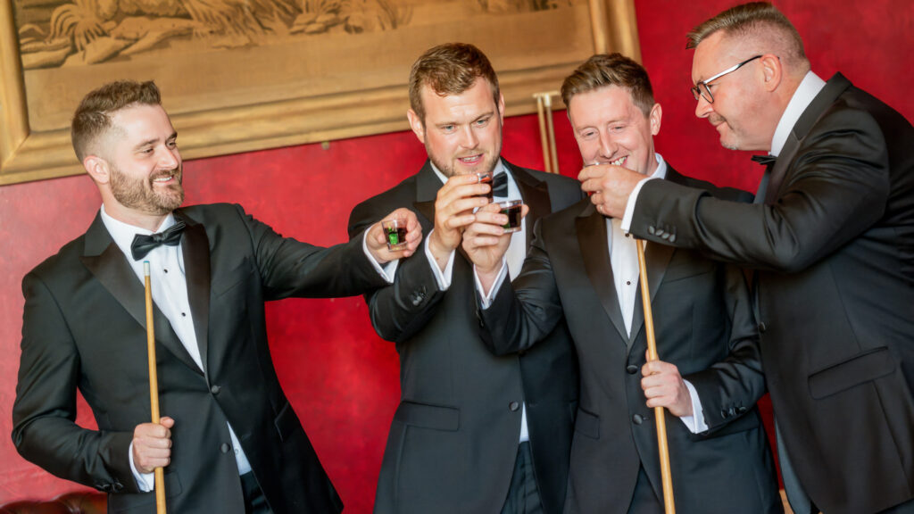 Men in tuxedos playing billiards and toasting. Allerton Castle wedding photographs