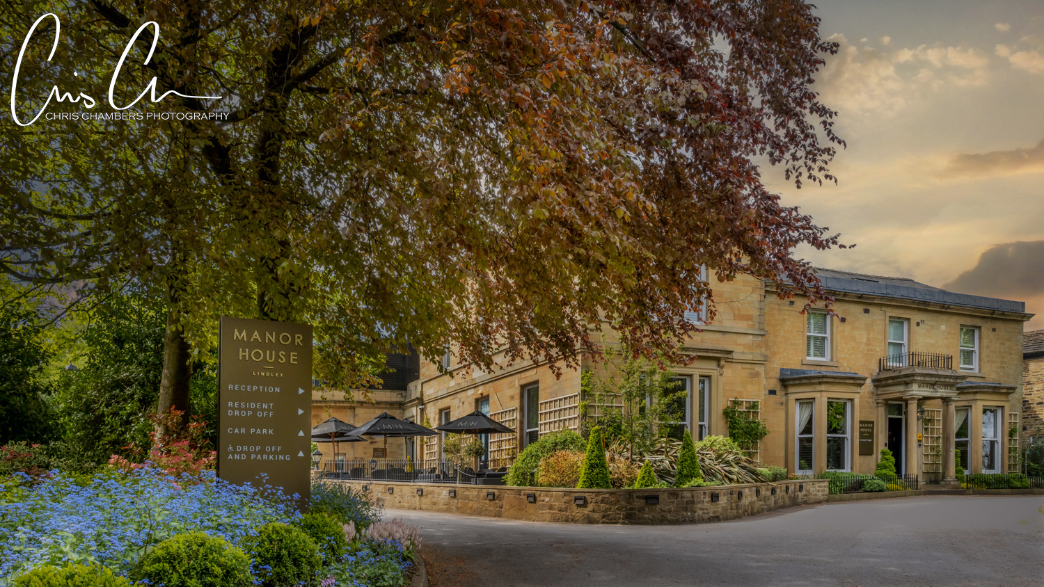 Manor House hotel entrance with blooming flowers at dusk.