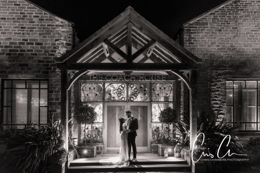Shabana and jonny embracing at illuminated Coach House entrance at night. Manor House Lindley wedding photography