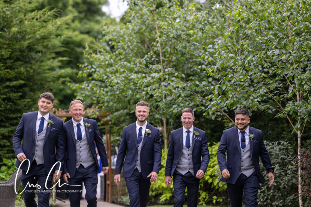 Groomsmen walking outdoors in formal wedding attire.
