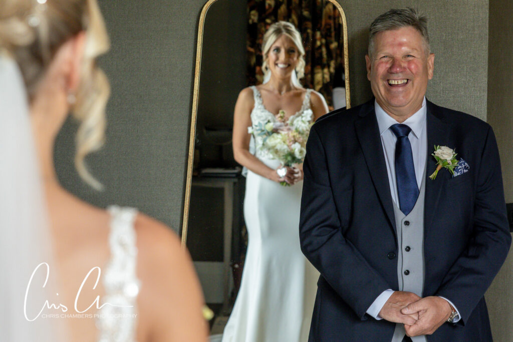 Father admiring bride in mirror, joyful wedding moment.